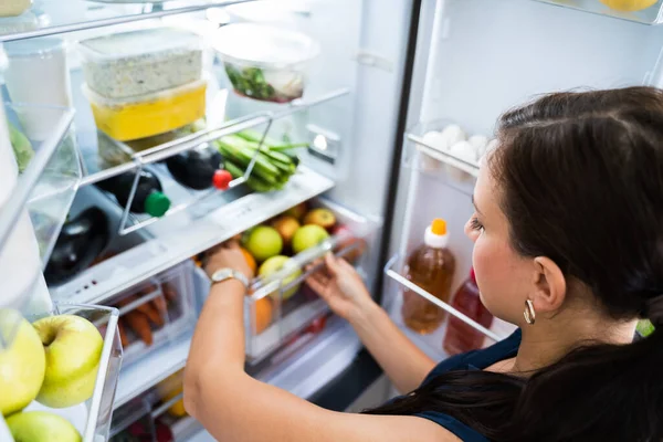 台所で冷蔵庫の中に食べ物を探している女性 — ストック写真