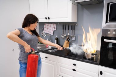 Mutfakta yanan tencereyi söndürmek için yangın söndürücü kullanan bir kadın.