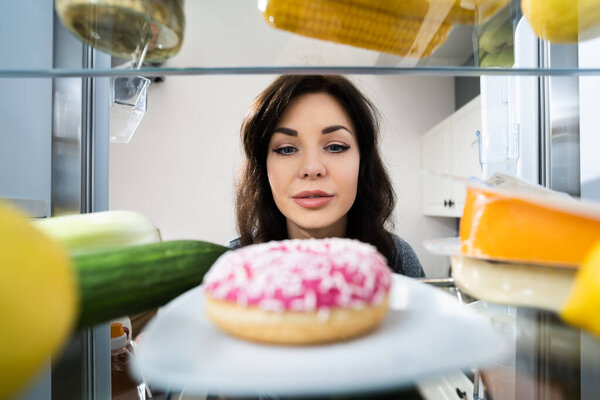 Happy Young Woman Looking At Donut From Refrigerator Or Freezer