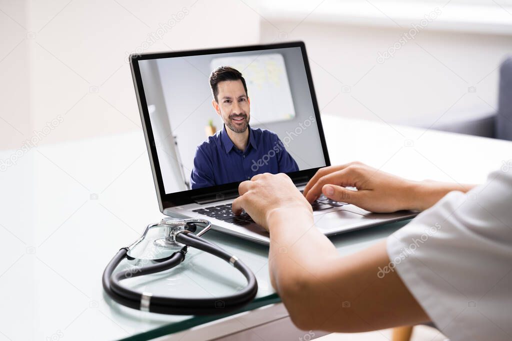 Doctor Talking To Male Patient Through Video Chat On Laptop At Desk