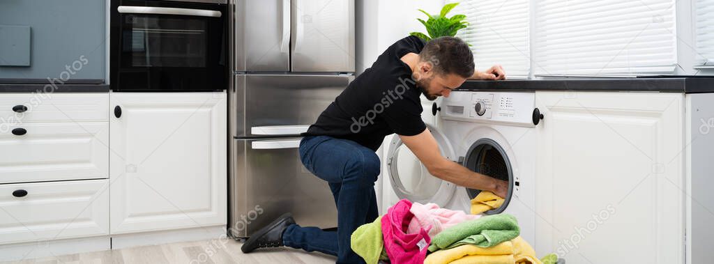 Man Loading Clothes Into Washing Machine In Kitchen