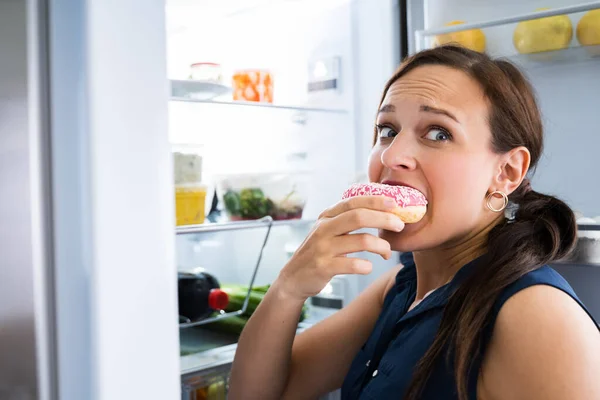 Fome Jovem Mulher Comer Donuts Perto Geladeira — Fotografia de Stock