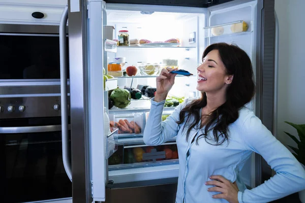 Junge Frau Isst Nachts Essen Der Nähe Des Offenen Kühlschranks — Stockfoto