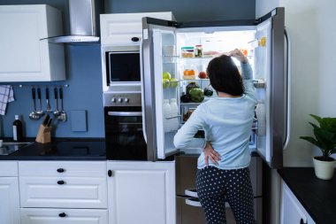 Confused Hungry Woman Looking In Open Fridge clipart