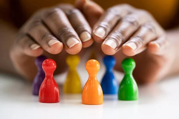 Diversity And Inclusion Concept. Hand Protecting Hand Colored Staff Pawns In Circle