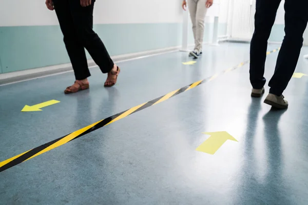 People In Office Following Social Distancing Tape Markings On Floor