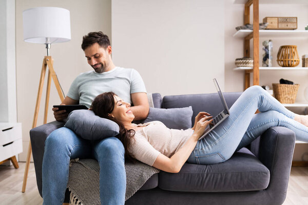 Family Couple Using Laptop And Tablet On Couch