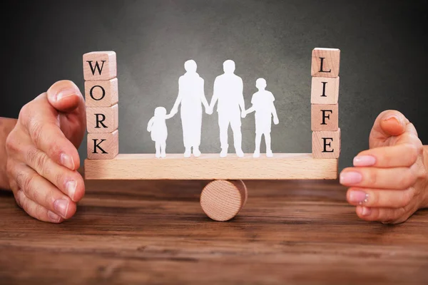 Human Figure Standing Between Work And Life Wooden Blocks On Seesaw Being Protected By Businessperson