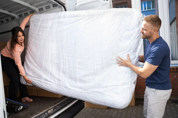 Couple Unloading Mattress From Van Or Truck While Moving House Outdoors