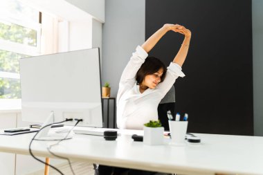 Kadın büro masasında geriniyor. Sandalye üzerinde esneme egzersizi