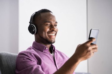 Mutlu Afrikalı Amerikalı adam kulaklıkla evde müzik dinliyor.