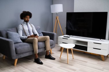 Evdeki akıllı telefonu kullanarak koltukta oturan genç adam.