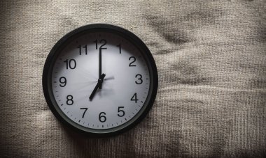 Basit kompozisyon, siyah duvar saat saat 7'de gösterilen bir yatak battaniye var.