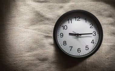 Basit kompozisyon, siyah duvar saat çeyrek geçmiş saat 9'da gösterilen bir yatak battaniye var. 