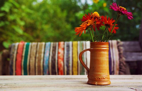 古い陶磁器のコップ古い木製のテーブル 背景にカラフルなカーペットに色とりどりの花 — ストック写真