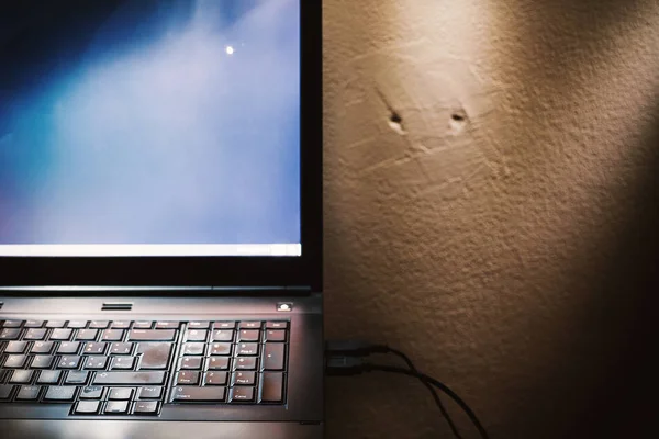 Dirty old laptop in front of an old wall interestingly illuminated.