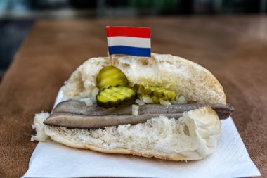 Geleneksel Hollanda Aperatif, ringa balığı, soğan ve turşu salatalık ile deniz ürünleri sandviçi. Ahşap masa haring Broodje. Hollanda bayrağı ile.