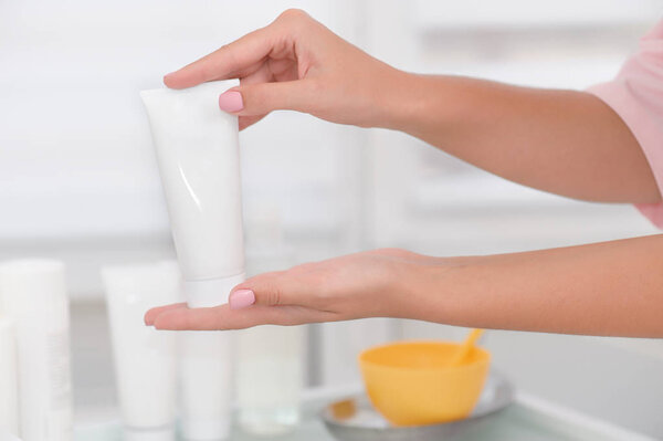 Hand skin care. Female hands holding cream tube, beautiful beautician woman hands with close-up over natural white background. Nails Beauty And Body Care Concept. Shallow DOF.