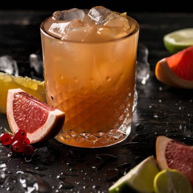 Bardak portakal suyu ve meyve dilimleri (portakal, greyfurt, limon ve Frenk üzümü) siyah arka plan üzerine buzla. Yakın çekim, sığ Dof, yumuşak odak.