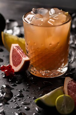 Bardak portakal suyu ve meyve dilimleri (portakal, greyfurt, limon ve Frenk üzümü) siyah arka plan üzerine buzla. Yakın çekim, sığ Dof, yumuşak odak.