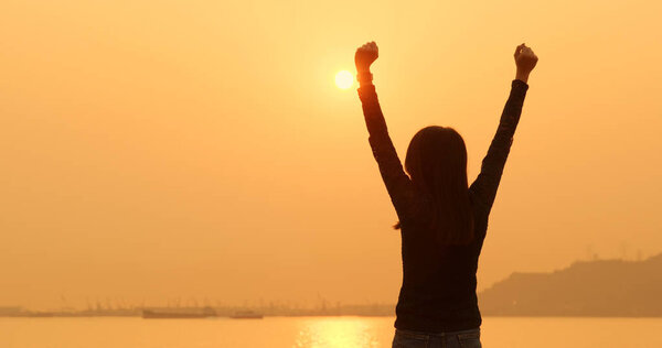 Woman raising hand up under sunset 