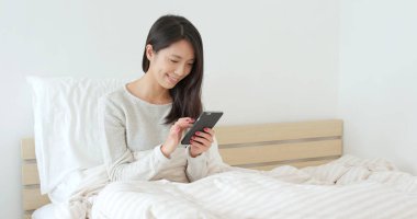 Yatakta akıllı telefon kullanan kadın.