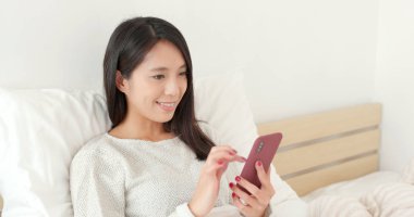 Yatakta cep telefonu kullanan kadın.