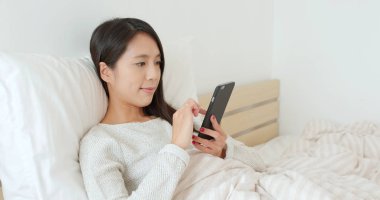 Yatakta cep telefonu kullanan kadın.