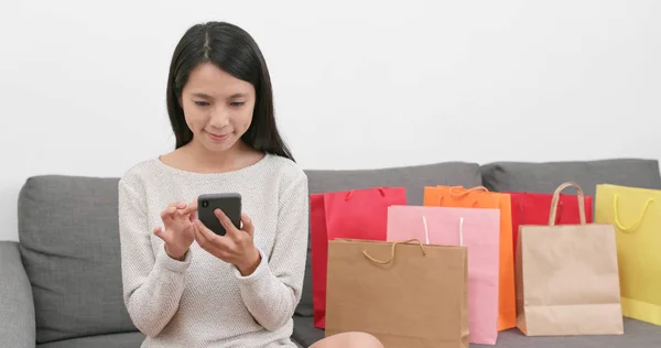 Woman using mobile phone with lots of shopping bags at home