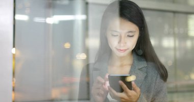 Şehir geceleri pencere yansıması ile Smartphone kullanarak iş kadını