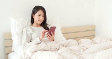 Yatakta cep telefonu kullanan kadın.