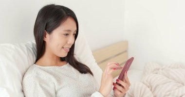 Yatakta cep telefonu kullanan kadın.