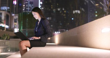 İş kadını gece şehirde dizüstü bilgisayarda çalışmak