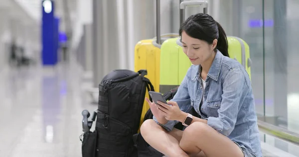 妇女使用手机在机场等待转机 坐在地板上 她的行李和背包 — 图库照片