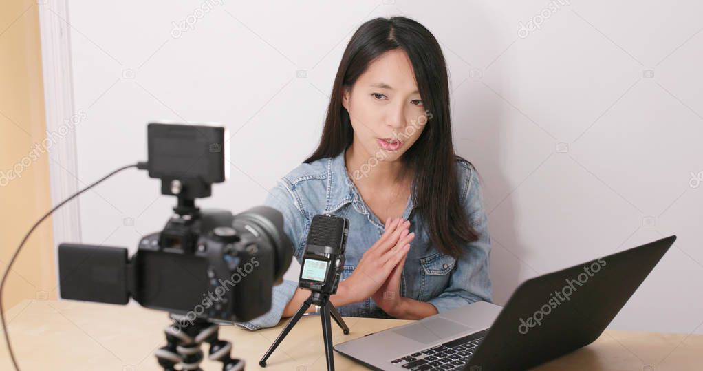 Woman talking in front of the digital camera with her notebook computer for making vlog at home