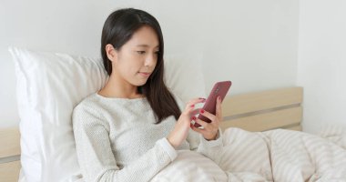 Yatakta cep telefonu kullanan kadın.