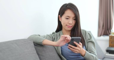 Evde akıllı telefon kullanan genç bir kadın.