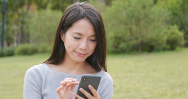 Parkta akıllı telefon kullanan genç bir kadın.