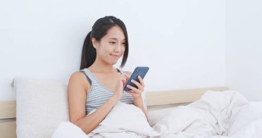 Yatakta cep telefonu kullanan kadın.