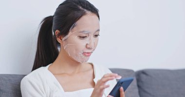 Akıllı telefon kullanan ve koltukta oturan bir kadın.