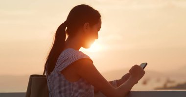 Günbatımı altında cep telefonu kullanan kadın