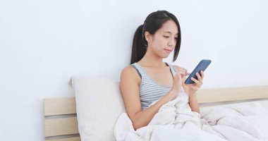 Yatakta cep telefonu kullanan kadın.