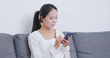 Akıllı telefon kullanan ve koltukta oturan bir kadın.