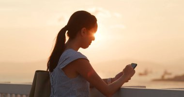 Günbatımı altında cep telefonu kullanan kadın