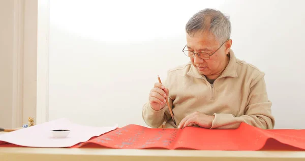 Old man writing Chinese calligraphy on red paper