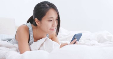 Yatakta akıllı telefon kullanan kadın.