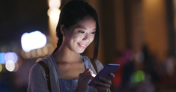 Woman searching on mobile phone in city at night