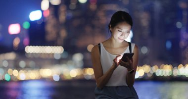 Gece şehirde akıllı telefon kullanan bir kadın.