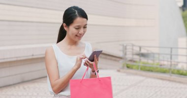 Kadın cep telefonu ve alışveriş çantası kullanıyor.