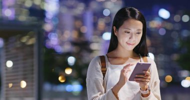 Gece şehirde akıllı telefon kullanan bir kadın.